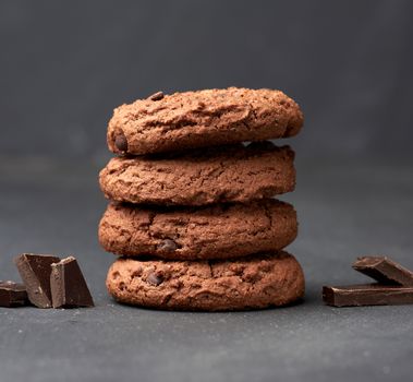 stack of baked round chocolate chip cookies and pieces of chocolate on a black table, close up