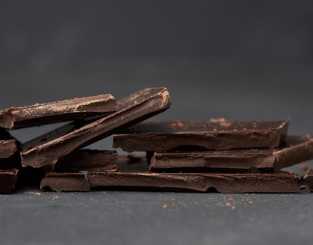 pieces of black chocolate on a black background, sweet dessert, close up