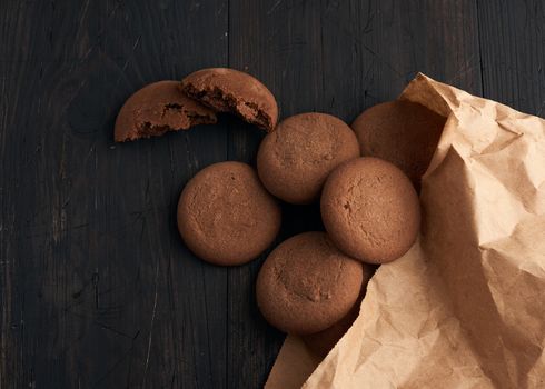 round chocolate chip cookies lie on a brown wooden table, dessert spilled out of a paper bag, top view