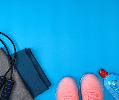 pink sport textile shoes and other items for fitness on a blue background, top view, copy space