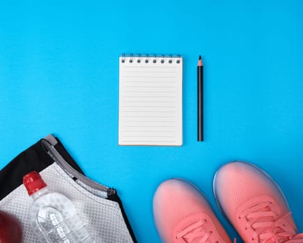 sports women's clothing for sports and fitness, top view, blue background, in the middle empty white sheets