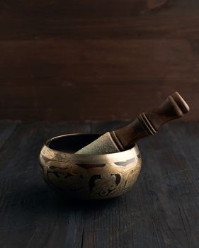 Tibetan singing copper bowl with a wooden clapper on a brown wooden table, objects for meditation and alternative medicine, close up