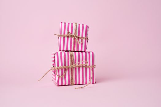 two boxes wrapped in pink paper and tied with a brown rope on a pink background, holiday backdrop 