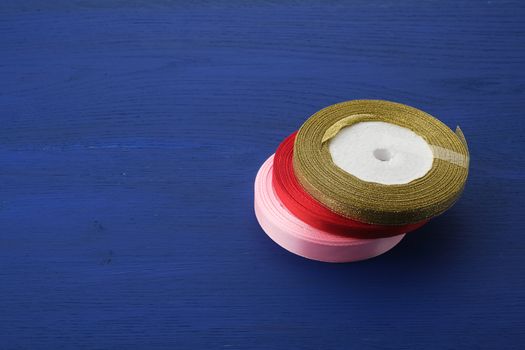 round bobbins with red, pink,  golden ribbon on a blue wooden background, top view
