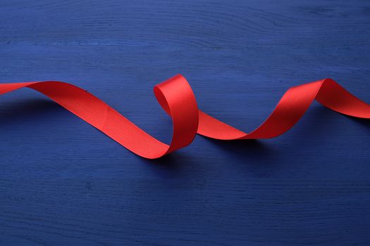 red silk thin ribbon twisted on a blue wooden background, trendy classic color, top view