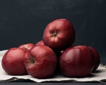 bunch of red ripe apples lies on a gray linen napkin, black background, close up