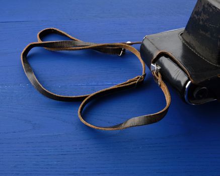 Vintage film camera in a leather case on a wooden blue background, close up