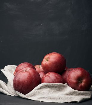 bunch of red ripe apples lies on a gray linen napkin, black background, close up