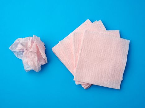 crumpled pink paper disposable napkins on a blue background, top view