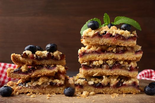 stack of square slices of baked crumble pie with blue plum on a wooden board, delicious dessert