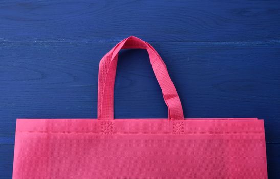 Reusable pink viscose bag on blue wooden background, plastic waste reduction concept
