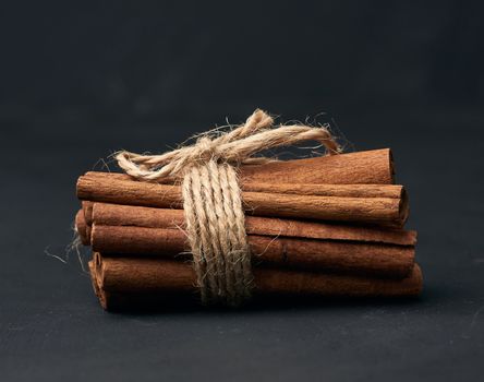tied bunch of brown cinnamon sticks on a dark background, close up