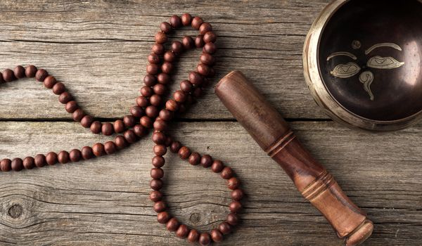 Tibetan singing copper bowl with a wooden clapper on a brown wooden table, objects for meditation and alternative medicine, top view