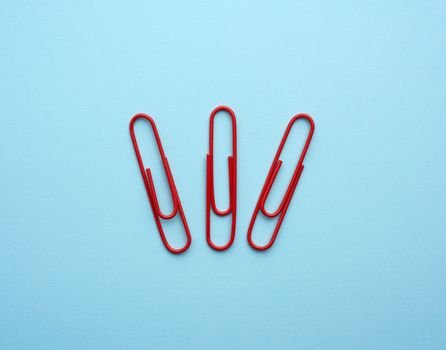 three metal red paper clips on a blue background, top view, close up