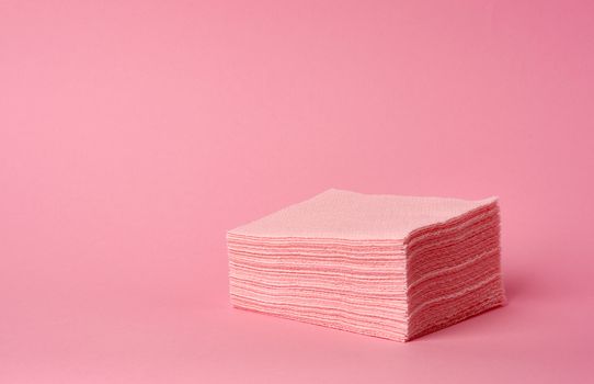 stack of paper disposable pink folded square napkins on a pink background, a place for inscription