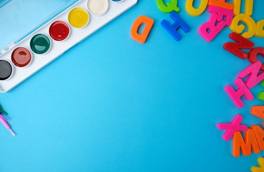 multicolored watercolor paints in a plastic box and brushes on a blue background, set for drawing, close up
