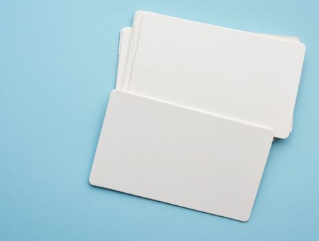 stack of rectangular white paper blank business cards on blue background, top view, close up