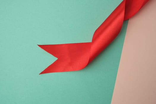 twisted silk red ribbon on a green-beige background, top view, cropped end