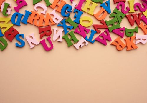 multi-colored wooden letters of the English alphabet on a beige background, top view, copy space