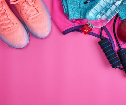 jump rope, bottle of water, pink sneakers, clothes for sports and fitness on a pink background, top view, flat lay