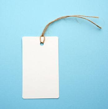 Blank white paper tag with white rope on a blue background. Price tag, gift, for writing address