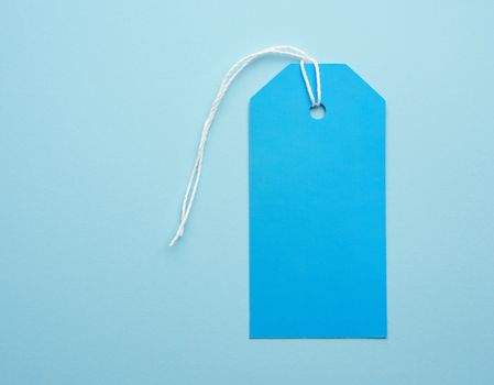 empty blue paper tag tied with white string. Price, gift, sale tag on the blue background, close up