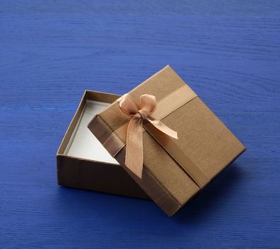 open brown square cardboard empty box, item lies on a blue wooden background, close up