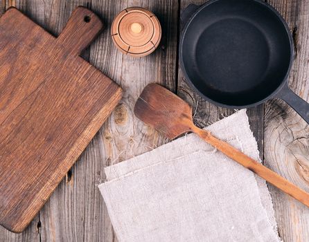empty black round cast iron pan with handle, wooden cutting board and knife on a gray table, top view