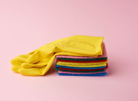 multi-colored kitchen sponge, rubber yellow gloves on a pink background, set of items for cleaning