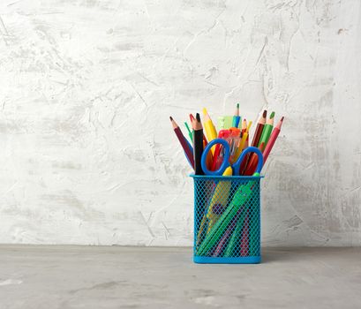 multicolored pens and pencils and other stationery in a blue metal holder, gray background