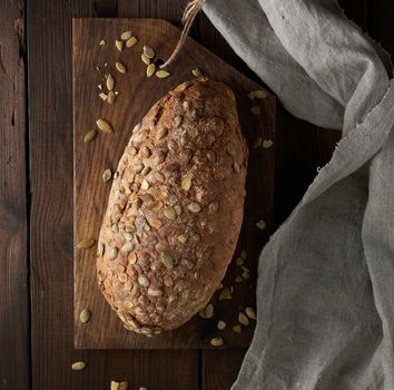 baked oval bread made from rye flour with pumpkin seeds on a gray linen napkin, top view