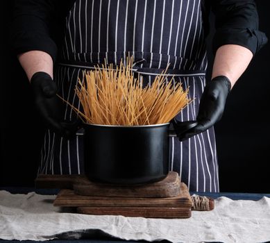 uncooked yellow long spaghetti in a black metal pan and a chef in a striped apron, cooking process