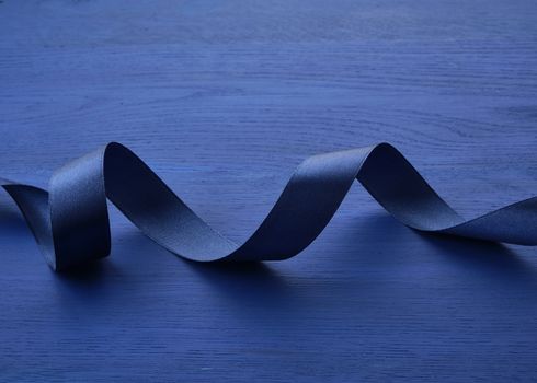 dark blue silk thin ribbon twisted on a blue wooden background, trendy classic color, top view