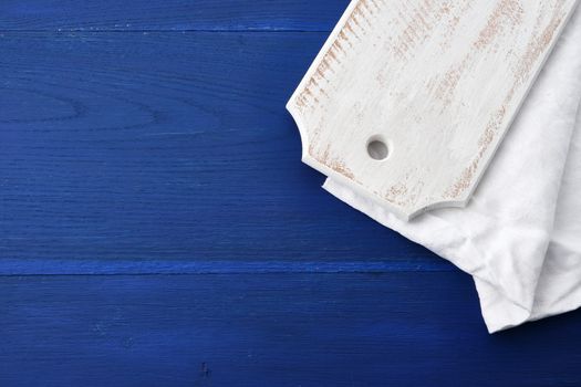 rectangular empty white kitchen cutting board and white textile towel on a blue wooden background from boards, top view