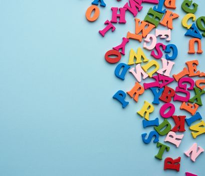 multi-colored wooden letters of the English alphabet on a blue background, top view, concept of back to school, copy space