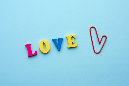 word love made of multi-colored wooden letters and a red paper clip in the shape of a heart on a blue background, top view