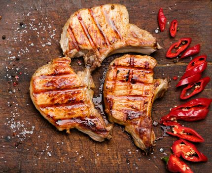 pork fried steak on the rib lies on a vintage brown wooden board, next to fresh red chili peppers, top view