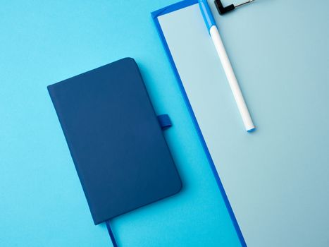 closed notebook and blue pen on a colored background, top view, flat lay