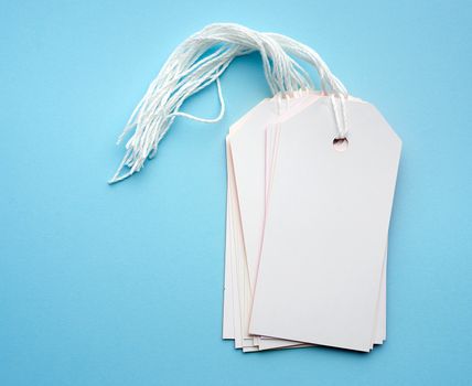 stack of empty white rectangular paper tags on a rope, blue background, item for luggage, price tag