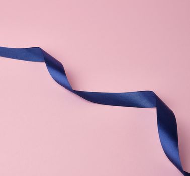 dark blue silk ribbon twisted into loops on a pink background, abstract background for the designer