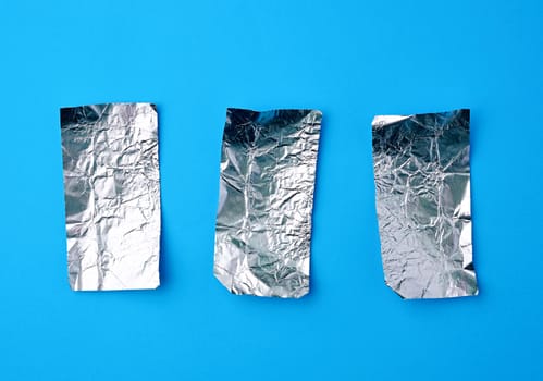 various crumpled foil used candy wrappers on a blue background, top view