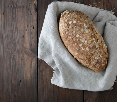 baked oval bread made from rye flour with pumpkin seeds on a gray linen napkin, top view