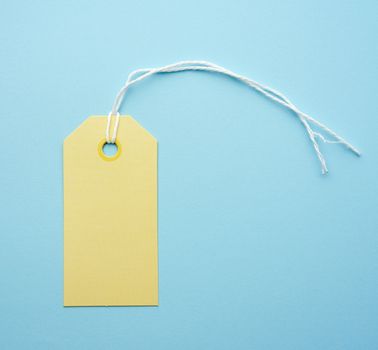 empty yellow paper tag tied with white string. Price, gift, sale tag on the blue background, close up