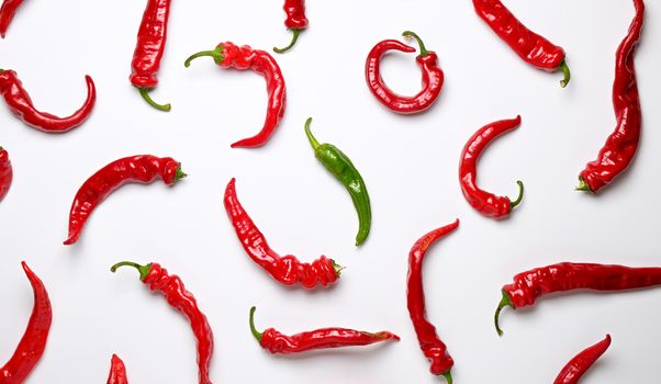 many red whole fruits of hot pepper and one green on a white background, concept of difference and discrimination