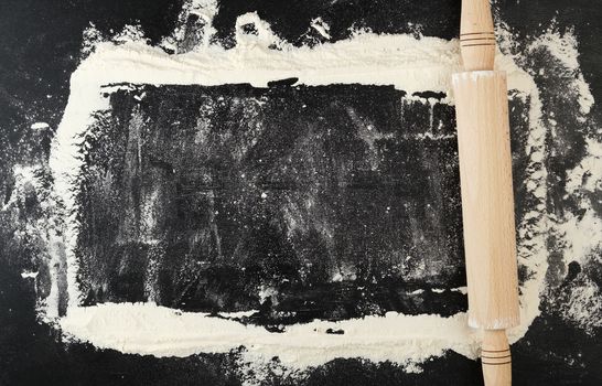 wooden rolling pin on a black background, top view, scattered white wheat flour