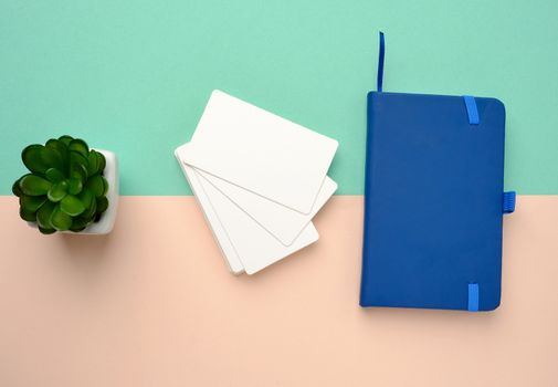 stack of rectangular white blank business cards and blue notebook on a green beige background, top view
