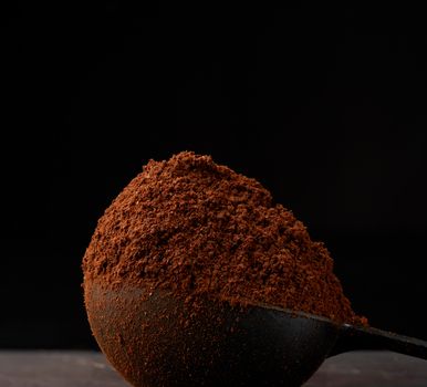 ground roasted coffee arabica in a spoon on a black background, close-up