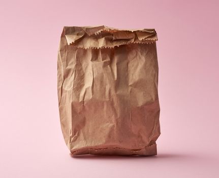 full paper disposable bag of brown kraft paper on a pink background, concept of rejection of plastic packaging, template for designer, packaging for contactless product delivery