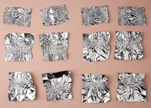 various crumpled foil used candy wrappers on a beige background, top view