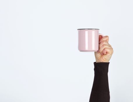 pink ceramic cup in a female hand on a white background, hand is raised up